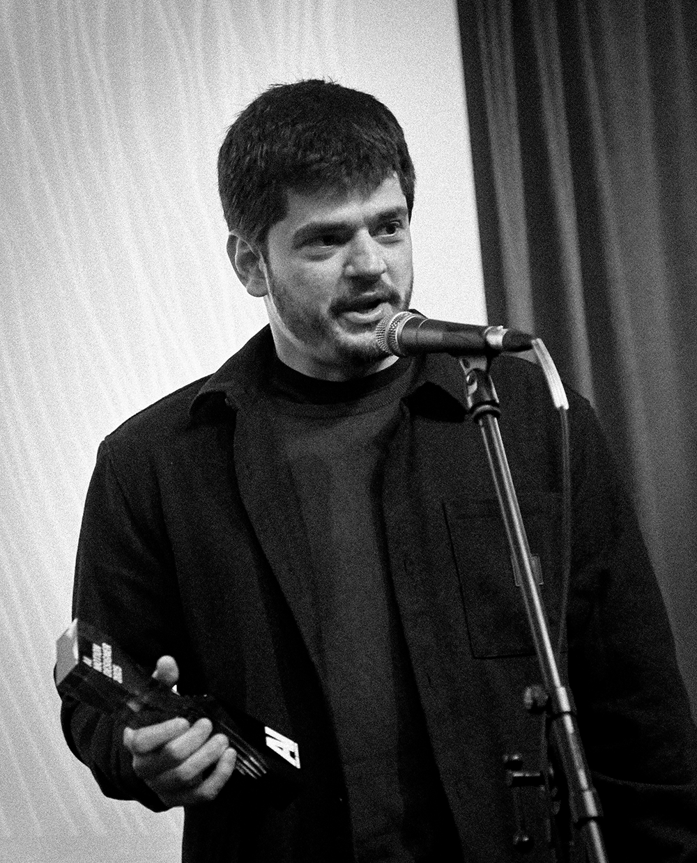 Marcello Costa on stage, speaking into a microphone and holding an award